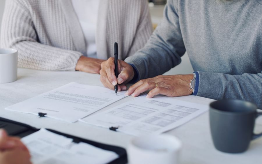 Two people sign documents at a white table with pens, papers and mugs.