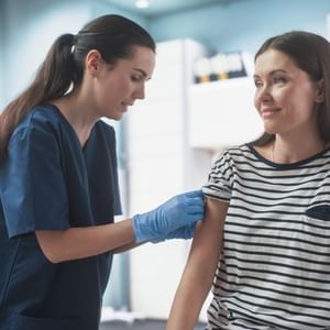 Healthcare worker in navy scrubs and gloves administers a shot to a patient.