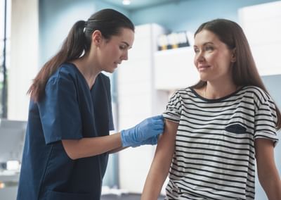 Healthcare worker in navy scrubs and gloves administers a shot to a patient.