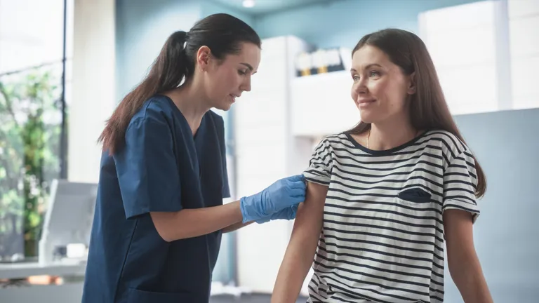 Healthcare worker in navy scrubs and gloves administers a shot to a patient.