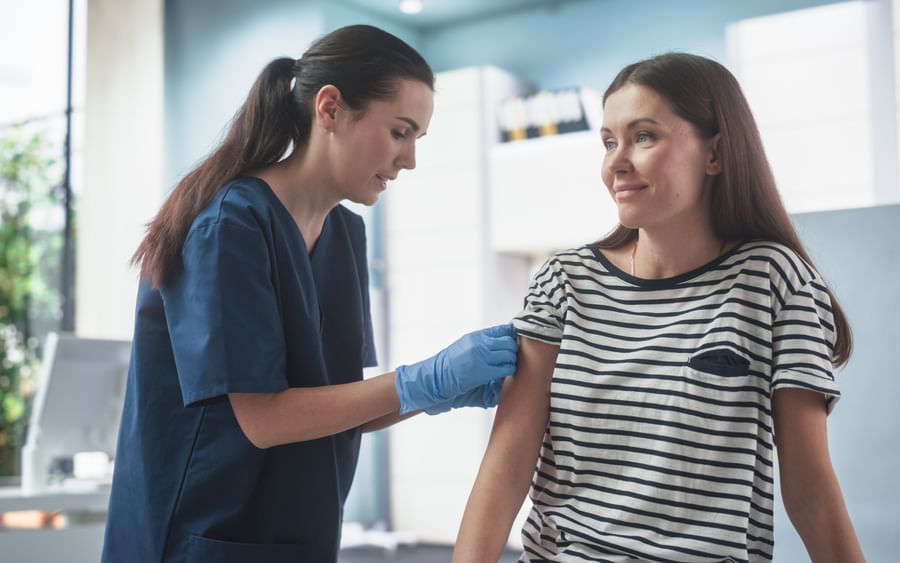 Healthcare worker in navy scrubs and gloves administers a shot to a patient.