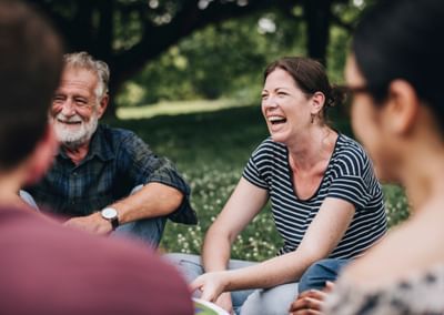A group of people laughing together outdoors in a sunny park.