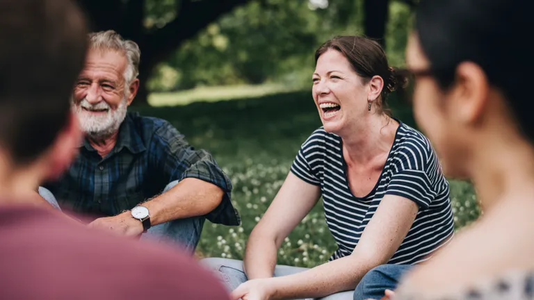 A group of people laughing together outdoors in a sunny park.