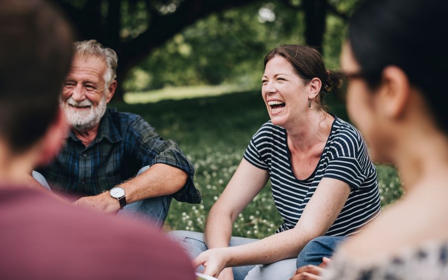 Group of adults sitting on the grass in a park, laughing and chatting together.