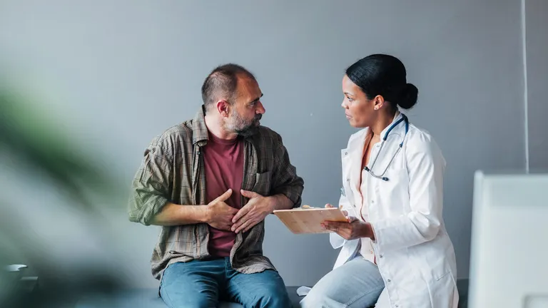 Three people sit on a sofa, examining a tablet together, against an orange wall.