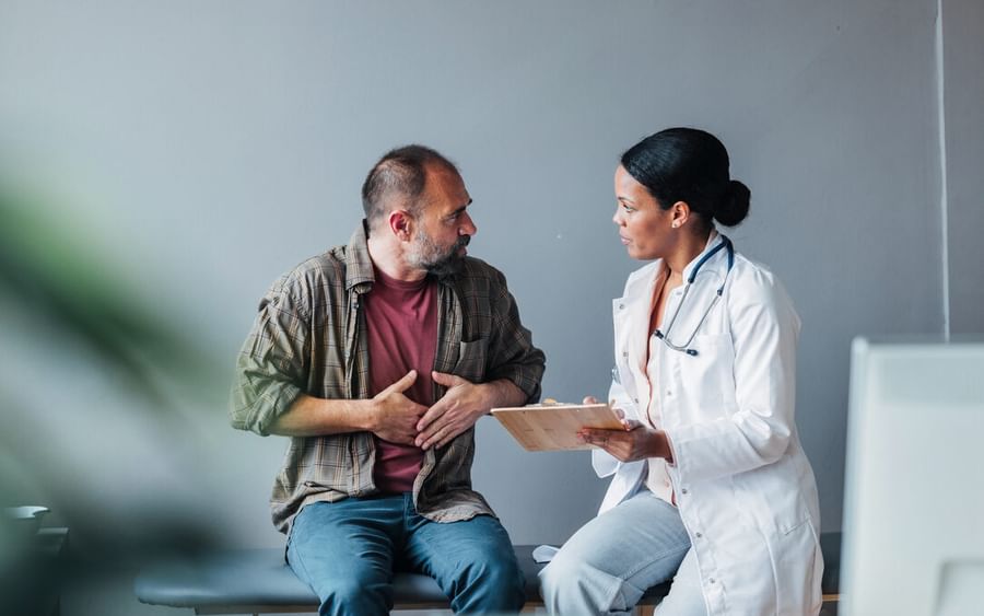 Three people sit on a sofa, examining a tablet together, against an orange wall.