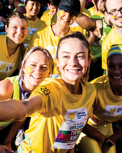 Diverse group in yellow Cancer Council shirts take a group selfie at a charity run.
