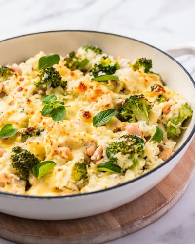 One pot cheesy chicken and broccoli rice in a deep white pan on a wooden mat.