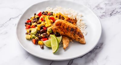 A white plate containing Cajun-style chicken, black bean salsa, rice and chopped vegetables