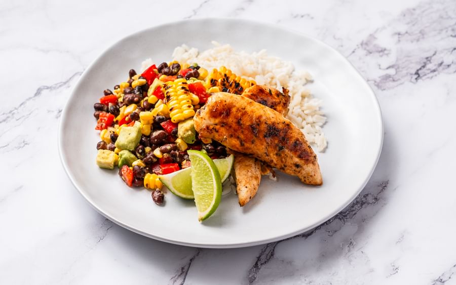 A white plate containing Cajun-style chicken, black bean salsa, rice and chopped vegetables