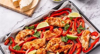 A baking tray filled with chicken and assorted vegetables, all covered in fajita seasoning