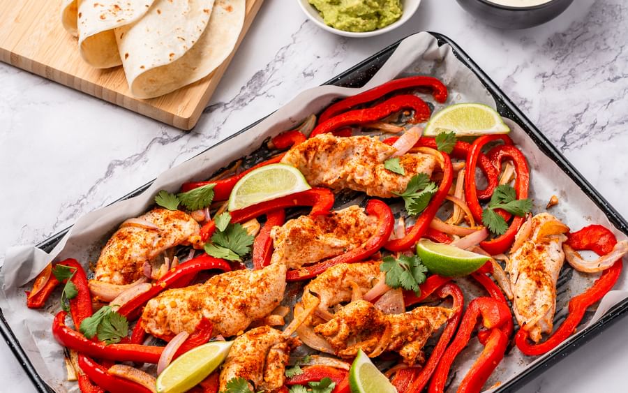 A baking tray filled with chicken and assorted vegetables, all covered in fajita seasoning