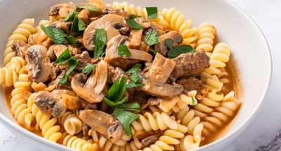 A white bowl containing spiral pasta mixed with a beef stroganoff sauce