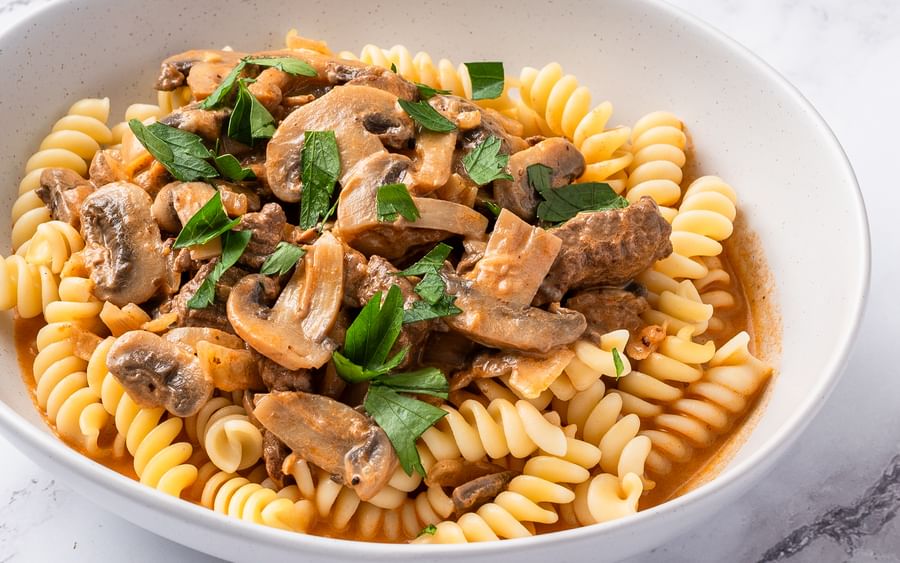 A white bowl containing spiral pasta mixed with a beef stroganoff sauce