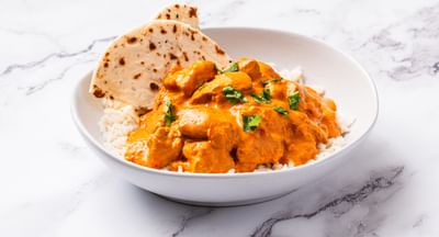 A bowl of butter chicken served with white rice and naan
