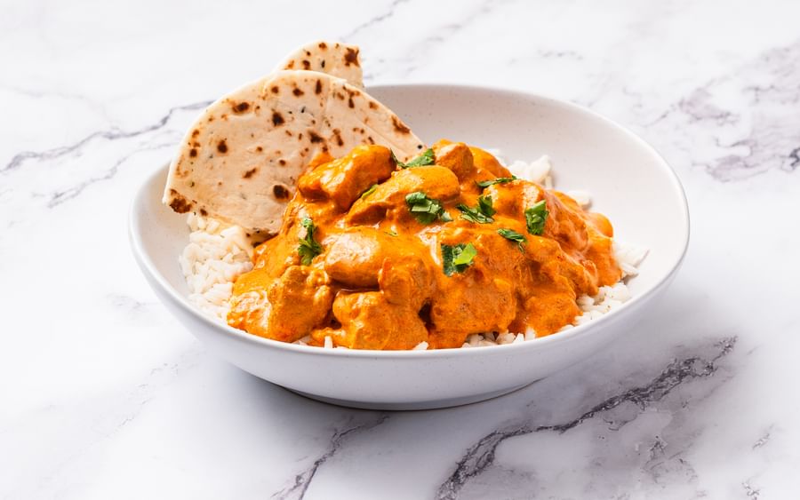 A bowl of butter chicken served with white rice and naan