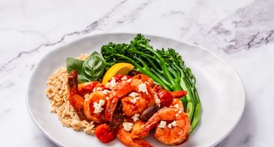 A plate of Mediterranean-flavoured prawns with broccolini, rice, cherry tomatoes and fresh basil