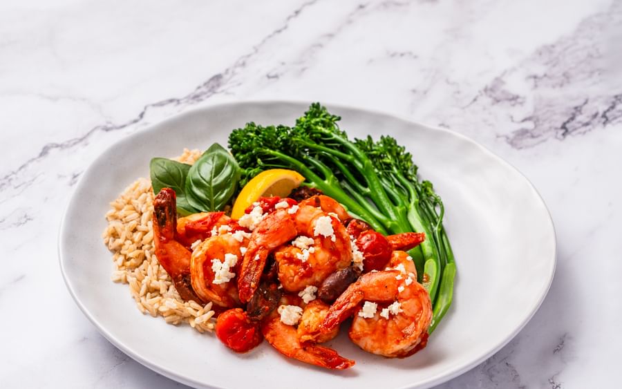 A plate of Mediterranean-flavoured prawns with broccolini, rice, cherry tomatoes and fresh basil