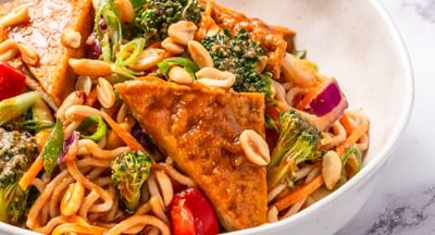 A white bowl filled with satay tofu, noodles and stir-fried vegetables