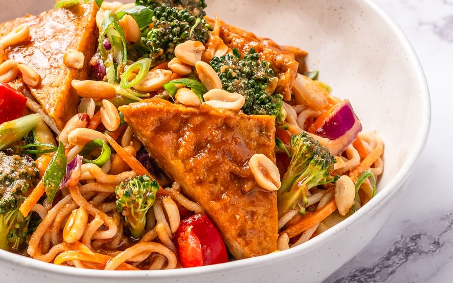 A white bowl filled with satay tofu, noodles and stir-fried vegetables