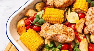 A white baking tray containing peri peri pork, corn, capsicum, cherry tomatoes and zucchini