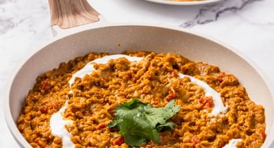 A pan filled with red lentil dahl and drizzled with plain yoghurt served alongside a plate of roti bread