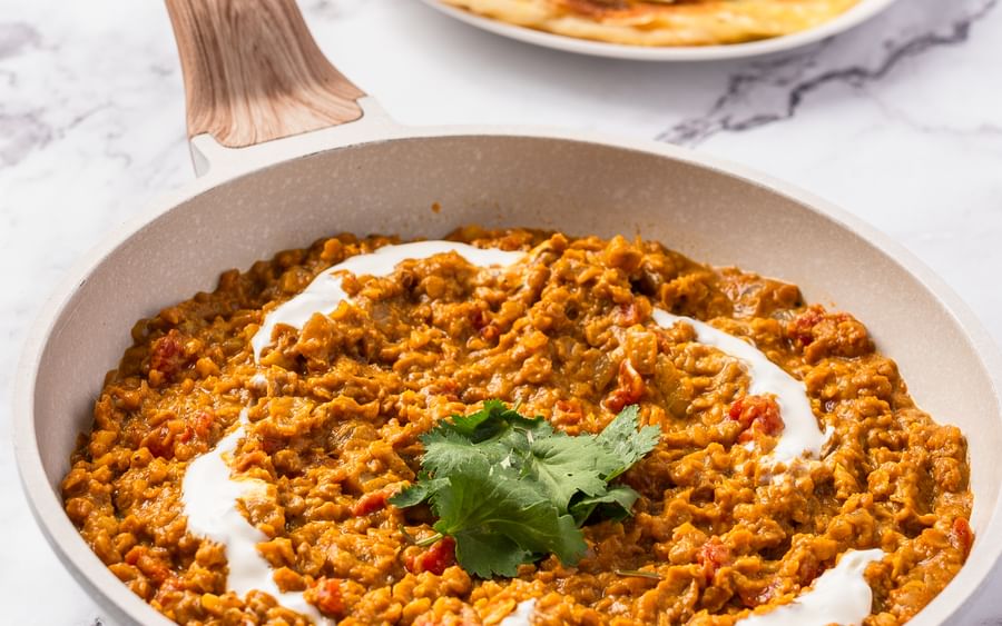 A pan filled with red lentil dahl and drizzled with plain yoghurt served alongside a plate of roti bread