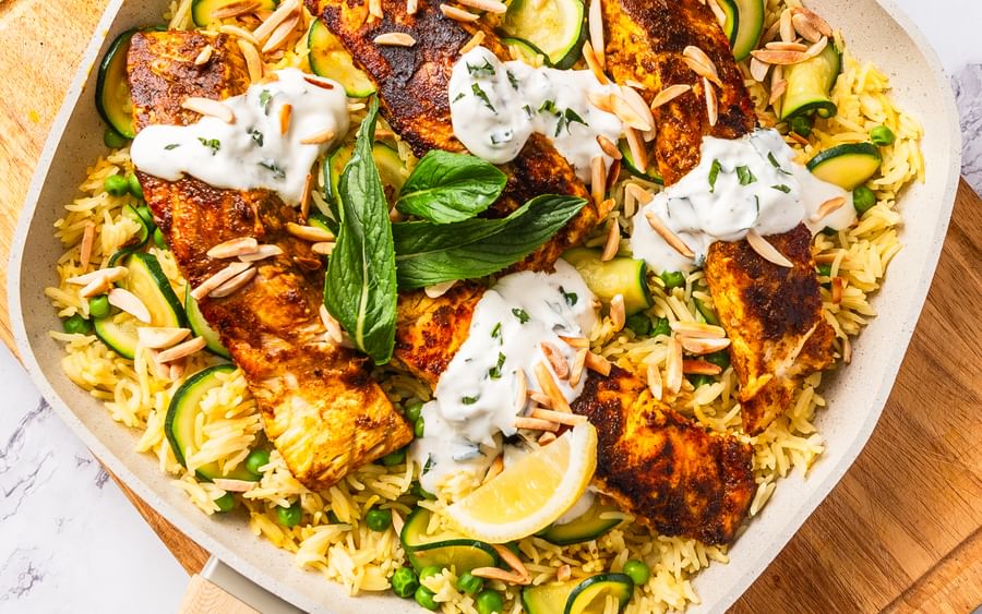 A one-pan tikka masala fish in a wide pan on a chopping board