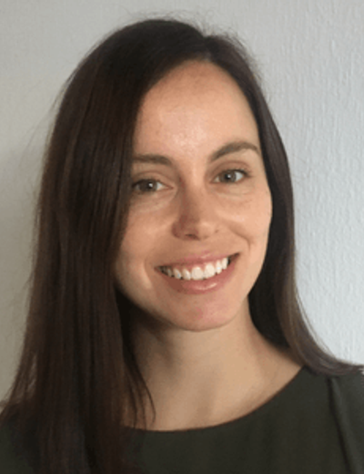 Person with long dark hair, smiling, wearing a dark sleeveless top, against a light wall.