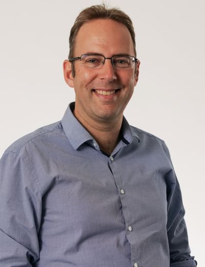 Person wearing a blue shirt and glasses, smiling against a plain light background.