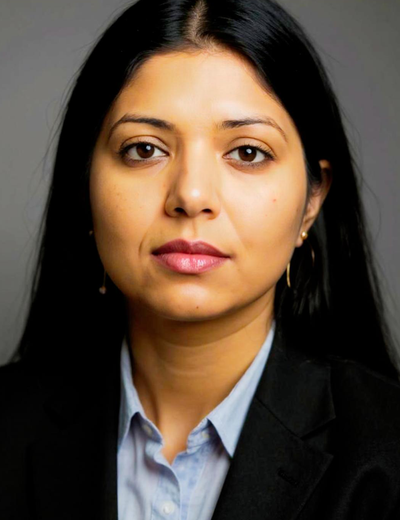 Portrait of a person with long dark hair, grey background, wearing a light blue shirt and black blazer.