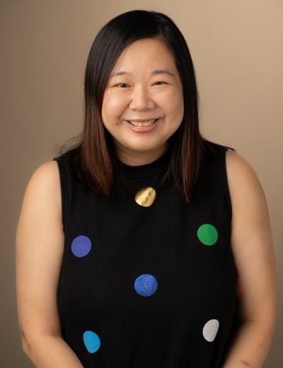 Smiling person with shoulder-length dark hair wearing a sleeveless top with colourful polka dots.