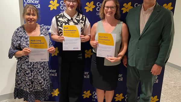 Four people stand in front of a Cancer Council SA backdrop, holding award certificates.