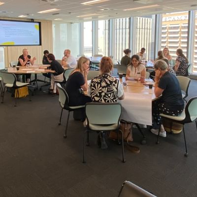 Diverse group in a bright conference room, seated at tables for a workshop.