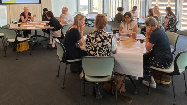 Diverse group in a bright conference room, seated at tables for a workshop.
