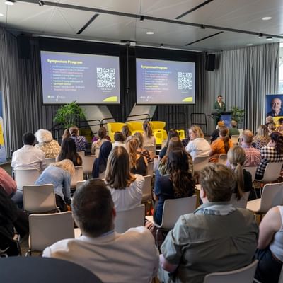 Looking over the back of a group of about 50 people sitting listening to Cancer Council SA's General Manger of Research and Support, Peter Diamond, speak at the podium.