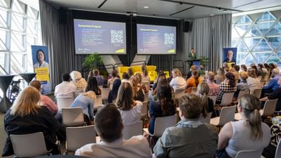 Looking over the back of a group of about 50 people sitting listening to Cancer Council SA's General Manger of Research and Support, Peter Diamond, speak at the podium.