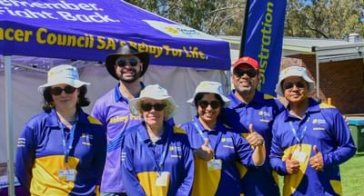 A group of six volunteers, all of different ages and genders, stand in front of a purple Cancer Council SA marquee