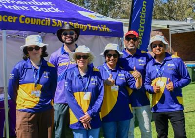 A group of six volunteers, all of different ages and genders, stand in front of a purple Cancer Council SA marquee
