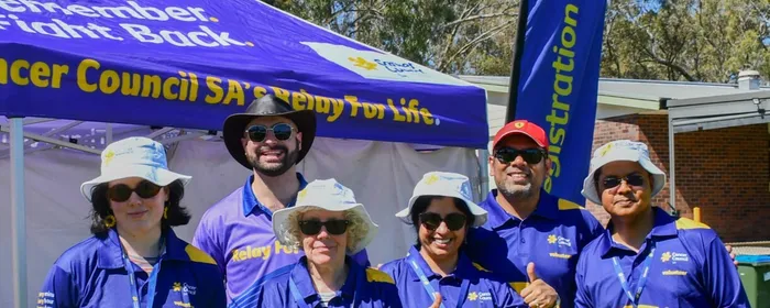 A group of six volunteers, all of different ages and genders, stand in front of a purple Cancer Council SA marquee