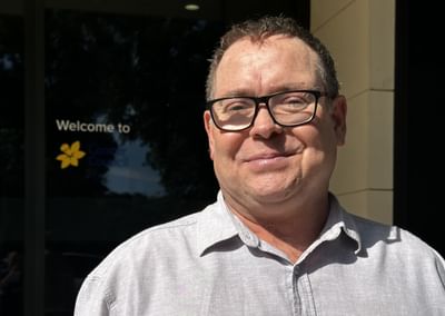 A man stands in front of a Cancer Council SA logo and smiles
