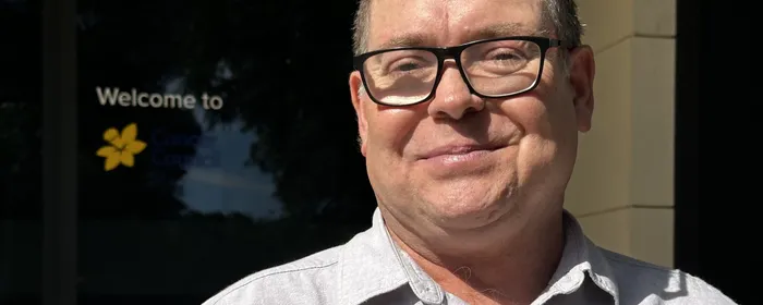 A man stands in front of a Cancer Council SA logo and smiles