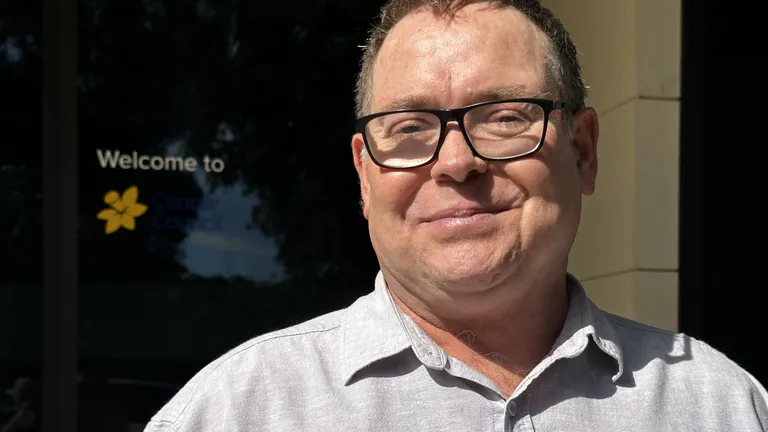A man stands in front of a Cancer Council SA logo and smiles