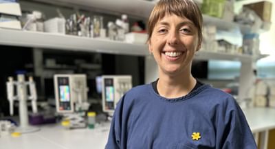 A female cancer researcher smiles at the camera in front of a table covered in laboratory research equipment