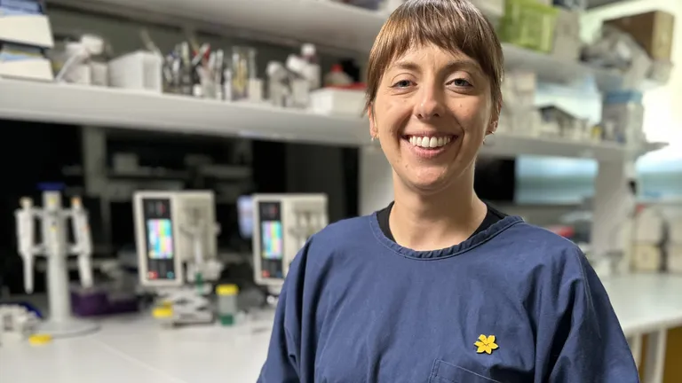 A female cancer researcher smiles at the camera in front of a table covered in laboratory research equipment