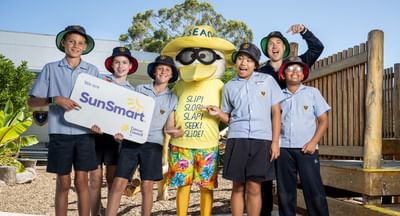 Sid the Seagull stands in the middle of a group of 6 primary school students, with the two students on the left holding a SunSmart sign