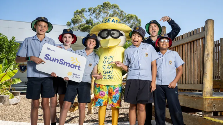 Sid the Seagull stands in the middle of a group of 6 primary school students, with the two students on the left holding a SunSmart sign