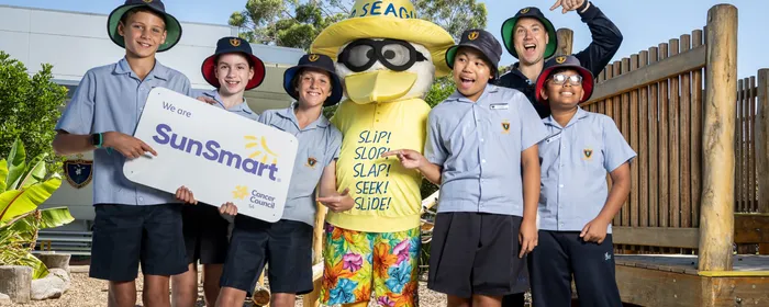 Sid the Seagull stands in the middle of a group of 6 primary school students, with the two students on the left holding a SunSmart sign