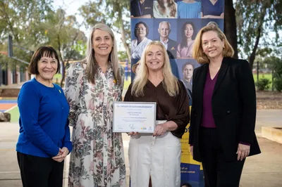 Four women stand in front of a Cancer Council SA banner at a school, celebrating the Shade Grants Initiative