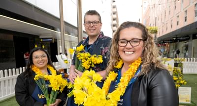 Three people hold daffodils to celebrate Daffodil Day in Adelaide's Rundle Mall in August 2026.